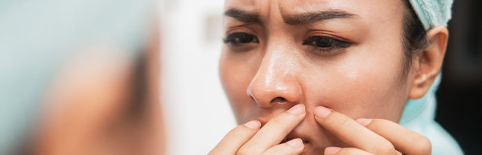 Woman in mirror squeezing blemish on face